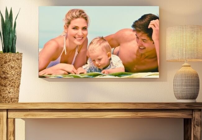 A canvas print hanging on the wall in a modern neutral living room. A mother and father sitting with their toddler looking at books by the pool.